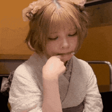 the girl is wearing a white kimono and holding her hand to her mouth .