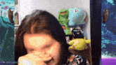 a woman covering her nose in front of stuffed animals including kermit