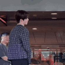 a young man in a plaid shirt is standing in a room with a man in a black shirt behind him .
