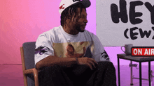 a man wearing a hat sits in front of a sign that says hey crew