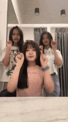 three girls are standing in front of a mirror making a heart shape with their hands