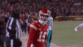 a football player in a red uniform with the number 15 on it is standing on the field with a referee .