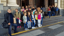 a group of children are standing on the steps of a building with a man standing behind them