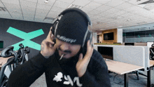 a man wearing headphones and a beanie has the letter x on his head
