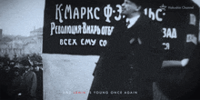 a black and white photo of a man standing in front of a sign that says " and tenin is young once again "