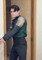 a man wearing a green vest and black pants is standing in front of a door