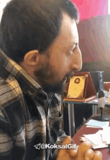 a man in a plaid shirt is sitting at a desk with a plaque in his mouth