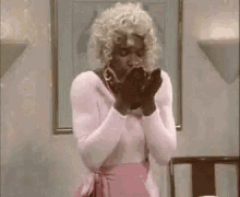a woman in a pink dress is praying with her hands folded in front of a chair .