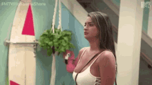 a woman in a white tank top is standing in front of a surfboard and holding a pink flamingo .