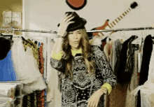 a woman wearing a hat is standing in front of a rack of clothes