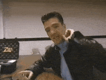 a man in a leather jacket is sitting at a desk with a box that says z1071 on it .
