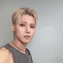 a young man with blonde hair is making a funny face while wearing a grey tank top .