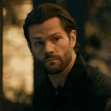 a man with a beard wearing a black shirt is looking at the camera