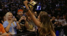 a woman is holding a championship belt in the air in front of a crowd .