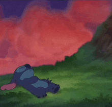 stitch is laying on the grass in front of a red cloudy sky .