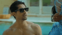 a shirtless man wearing sunglasses is standing next to a woman .