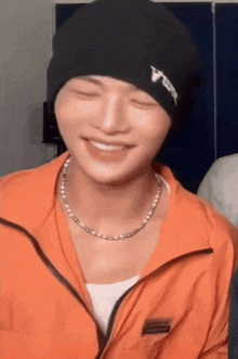 a man wearing a black beanie and an orange jacket is smiling