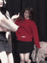 a woman in a red sweater and a black skirt is dancing on a stage .