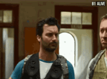 a man with a beard is standing next to another man with the words 81 alive on the bottom