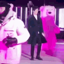 a man in a black coat is standing next to a pink teddy bear costume .