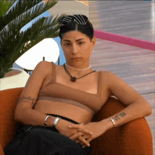 a woman in a crop top sits in a chair with her hands folded