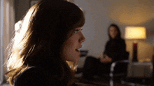 a woman sitting in a chair talking to another woman in a dark room