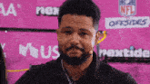 a man with a beard is standing in front of a pink backdrop that says nfl