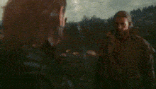 a man in a trench coat is standing in a field with a gun in his hand .