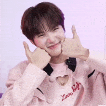 a young man wearing a pink jacket and a pink shirt with a heart cut out on the chest is giving a thumbs up .
