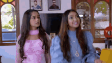 two girls are standing next to each other in a living room and looking at something .