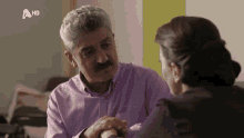 a man in a purple shirt is talking to a woman with a hd logo on the bottom right