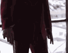 a man in a red suit is standing in front of a window with his hands in his pockets .