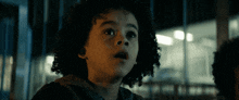 a young boy with curly hair is looking at something in the dark