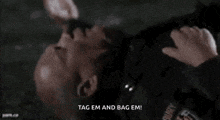 a bald man is laying on the ground with the words `` tag em and bag em '' written on the bottom .