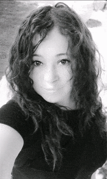 a black and white photo of a woman with long curly hair taking a selfie .