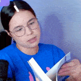 a woman wearing glasses and a blue shirt is holding a book