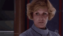 a woman with short blonde hair is wearing a turtleneck and a necklace and looking at the camera .