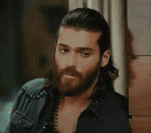 a man with long hair and a beard is wearing a black shirt .