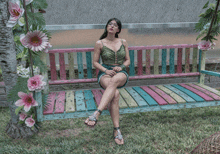 a woman sits on a colorful bench with flowers hanging from it