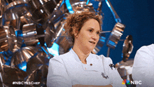 a woman in a chef 's uniform is sitting with her arms crossed on a nbc advertisement