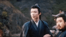 a man in a traditional costume is standing next to another man in a traditional costume in front of a mountain .