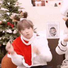 a man in a santa claus costume is dancing in front of a christmas tree .