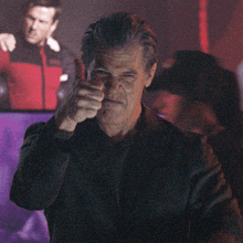 a man giving a thumbs up in front of a picture of a man in a red jacket