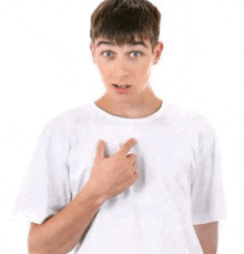 a young man wearing a white t-shirt is pointing at his chest .