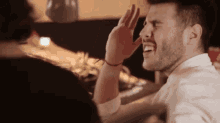 a man with a beard is laughing and covering his face with his hand