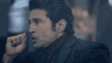 a man in a suit and red turtleneck is making a funny face while talking on a cell phone .