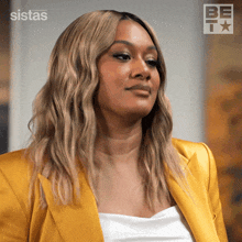 a woman wearing a yellow jacket is standing in front of a sistas logo