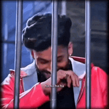 a man in a red jacket is laughing behind bars in a jail cell .