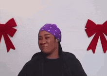 a woman wearing a purple bandana and a black jacket is standing in front of a wall with red bows .