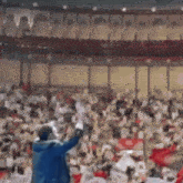 a man in a blue jacket is standing in front of a crowd in a stadium with his arms in the air .
